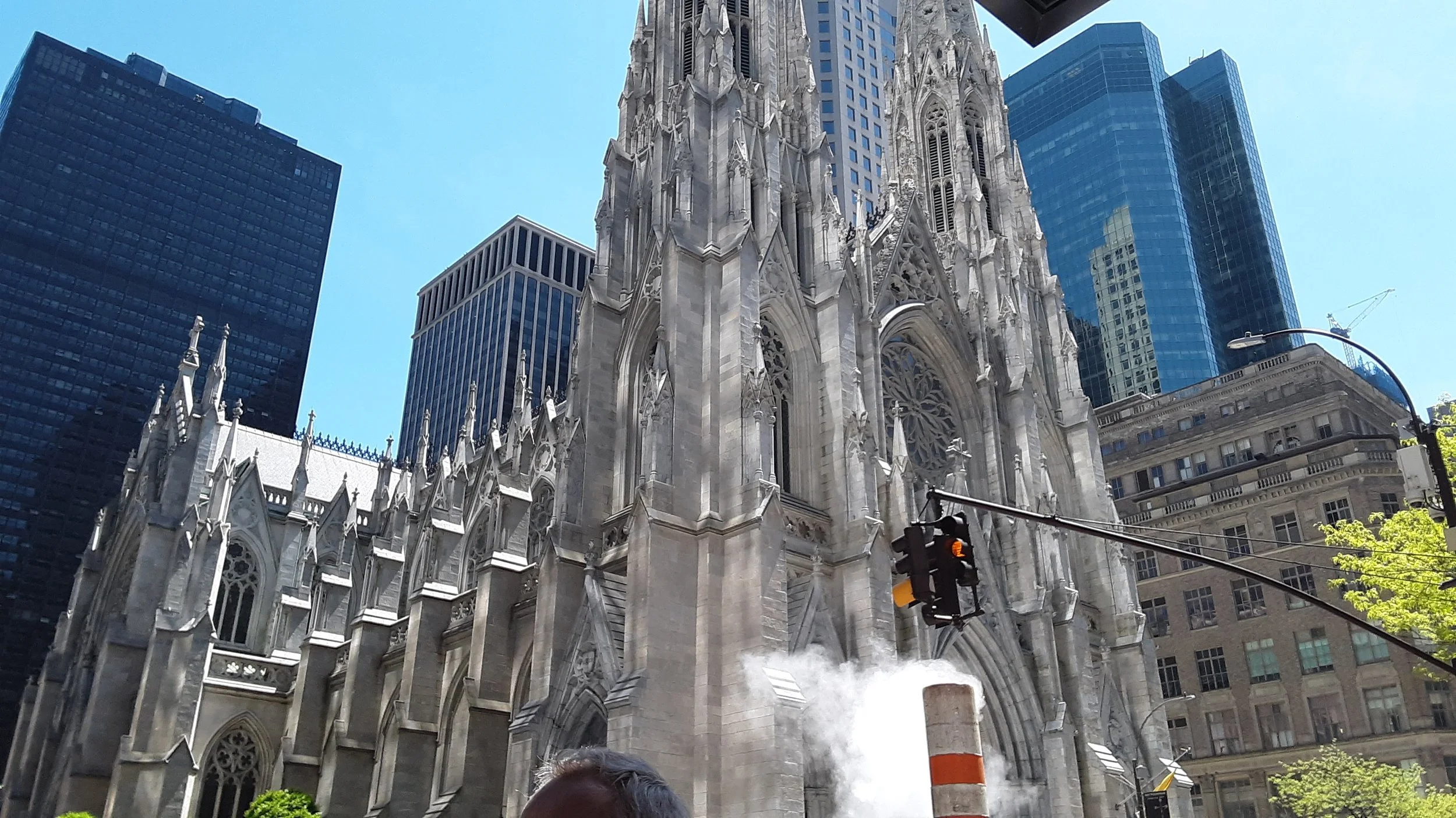 View of a historic Gothic-style cathedral with tall spires, surrounded by modern glass skyscrapers in an urban cityscape.