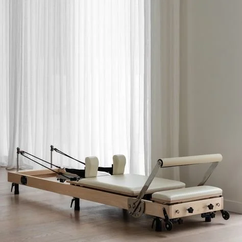 Physical therapy or Pilates reformer machine in a bright, minimal room with white curtains.