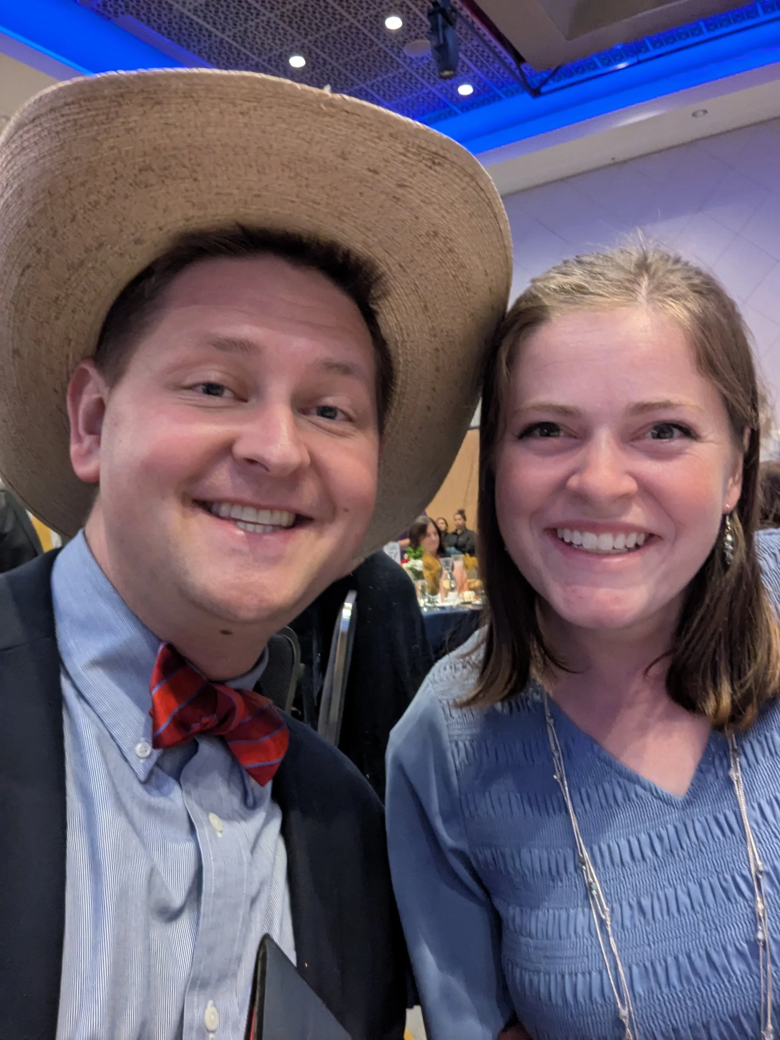 A man in a cowboy hat and a woman are dressed fancy and smiling together