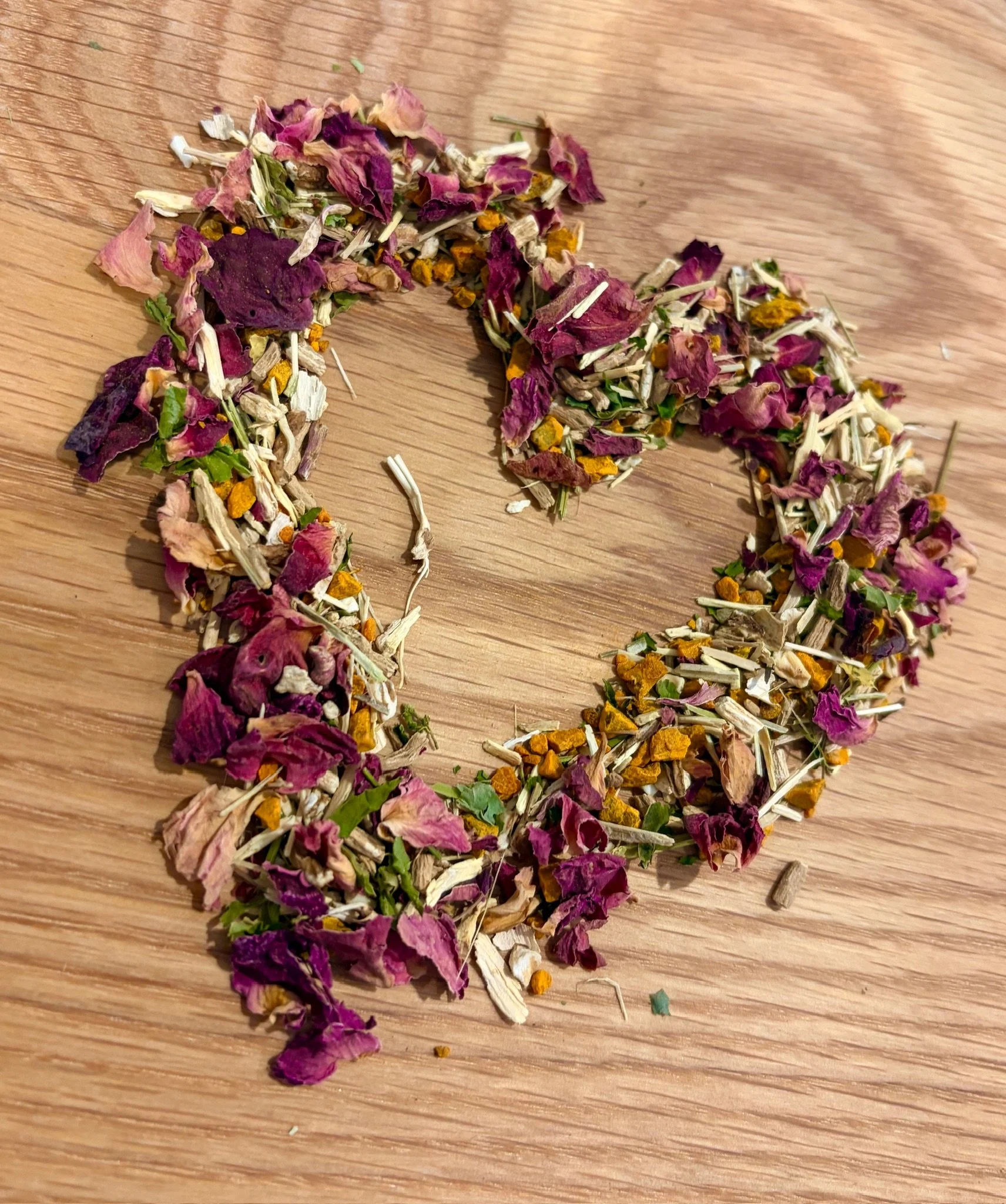 Loose dried flower petals, including purple, pink, white, yellow, and green, scattered on a wooden surface.