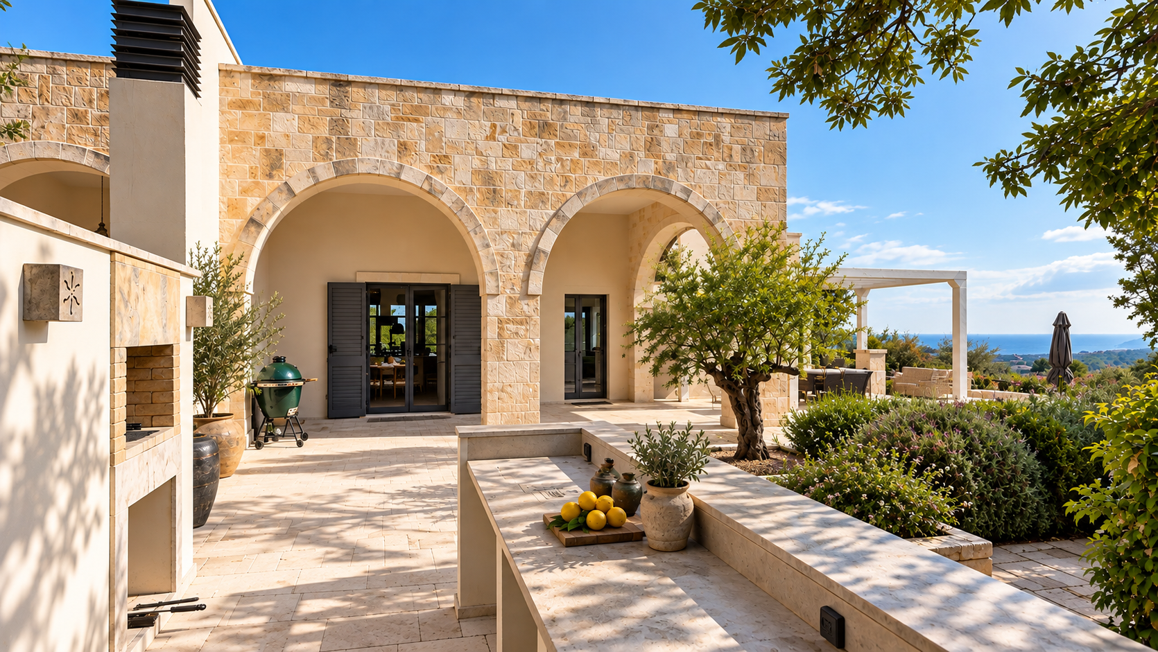 Outdoor patio area of a house with stone walls, arched doorways, potted plants, a lime and lemon display, furniture, and a view of the ocean in the distance.