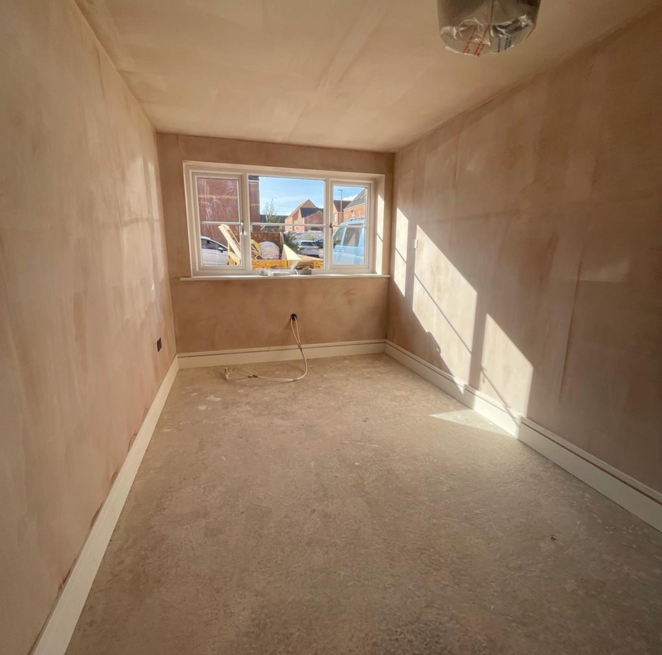 Empty room with unfinished floors, beige walls, a window, and some construction materials outside.