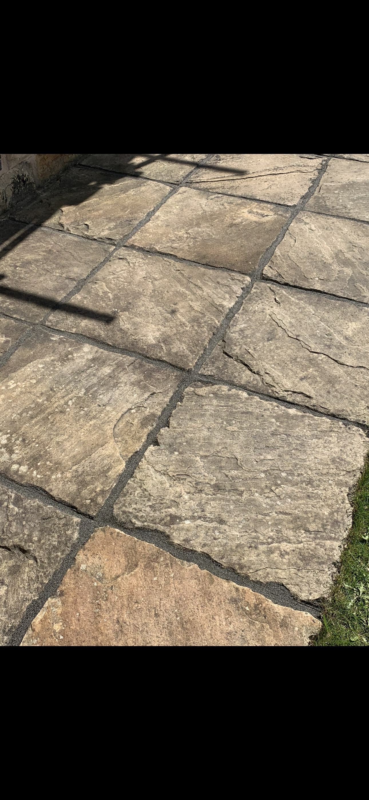 Close-up of a stone patio with large irregularly shaped stones and gray mortar, with a small section of grass visible on the right side.