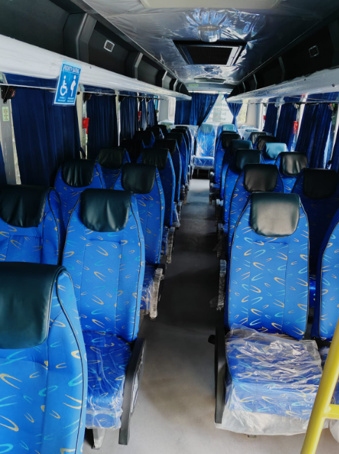 Empty passenger bus interior with blue seats, blue curtains, overhead storage, and a sign indicating wheelchair accessibility.
