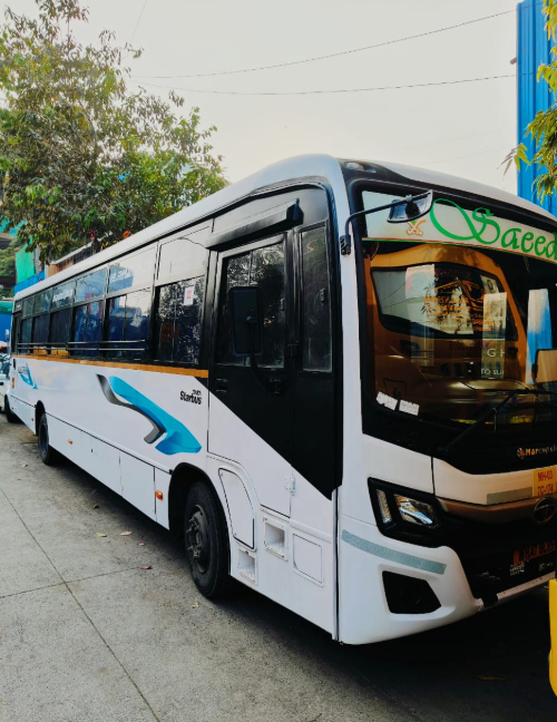 A white bus with black windows and blue and black accents parked on a street, with trees and a building visible in the background.