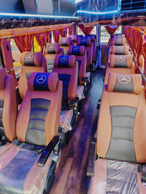 Interior of a bus with rows of beige and black seats featuring Mercedes-Benz logos on the headrests, red curtains, and colorful lighting. Push-back seat Force/Tempo Traveler 20 seater