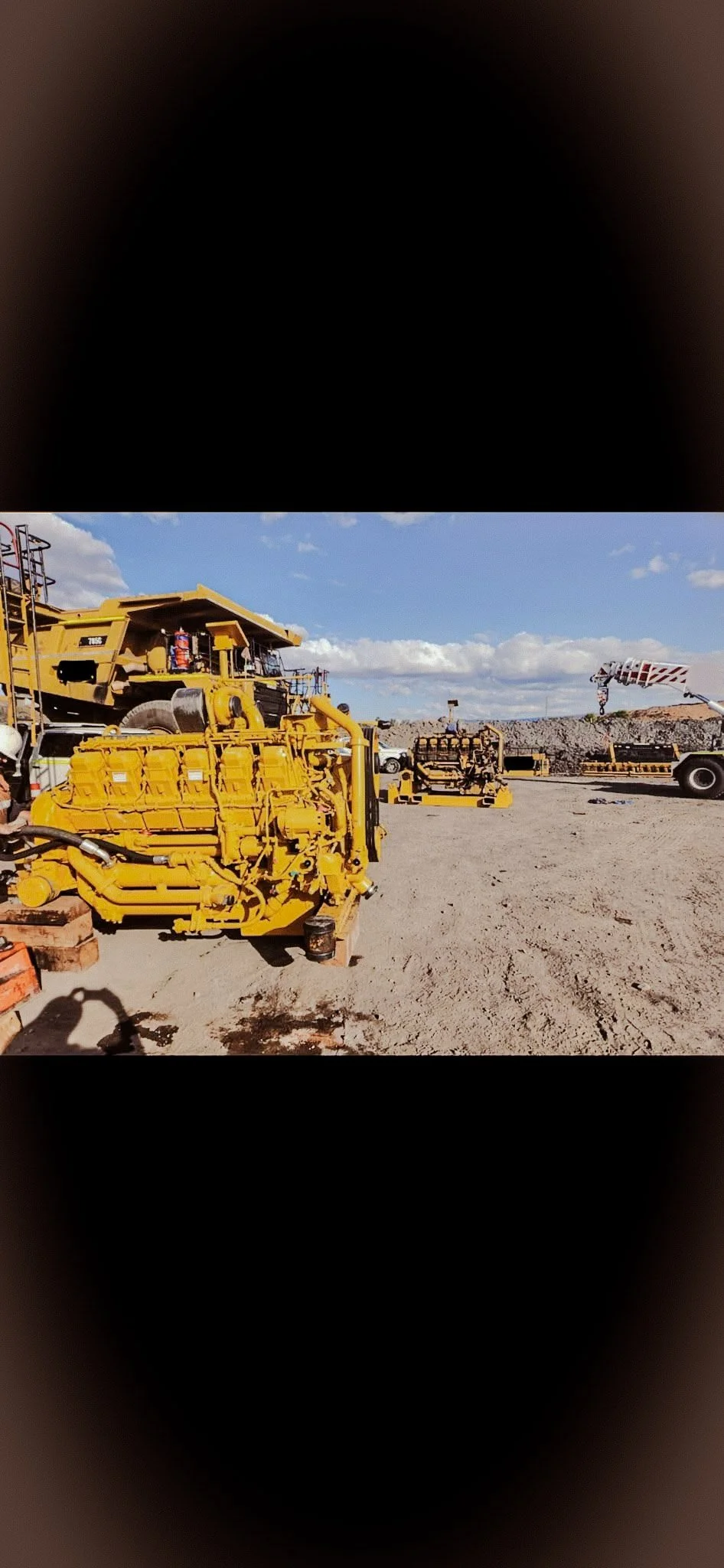 Construction site with large yellow machinery, including a bulldozer and heavy equipment, under a blue sky with scattered clouds.