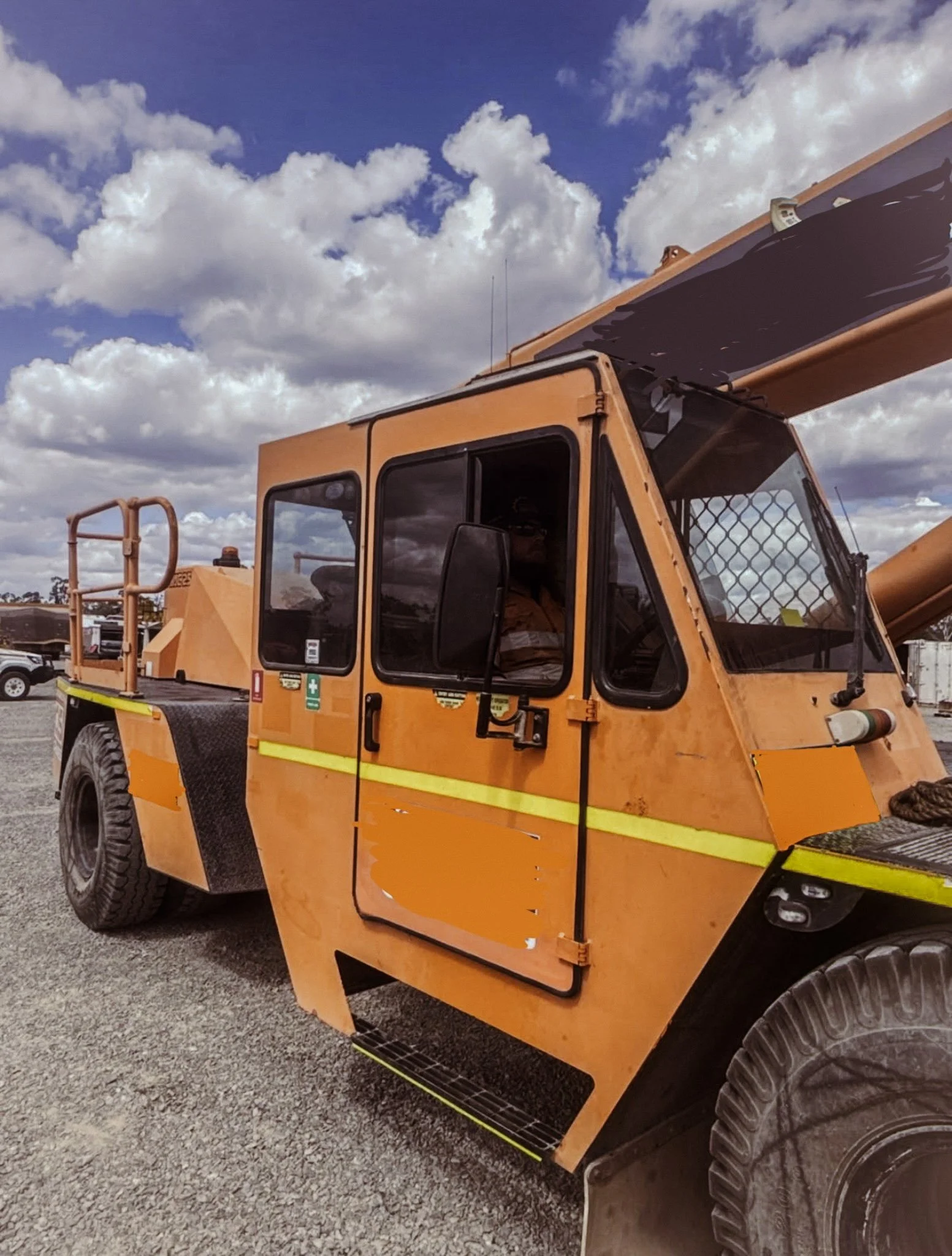 Close-up of a yellow construction vehicle with a black glass cabin and large tires, parked on gravel under a partly cloudy sky.