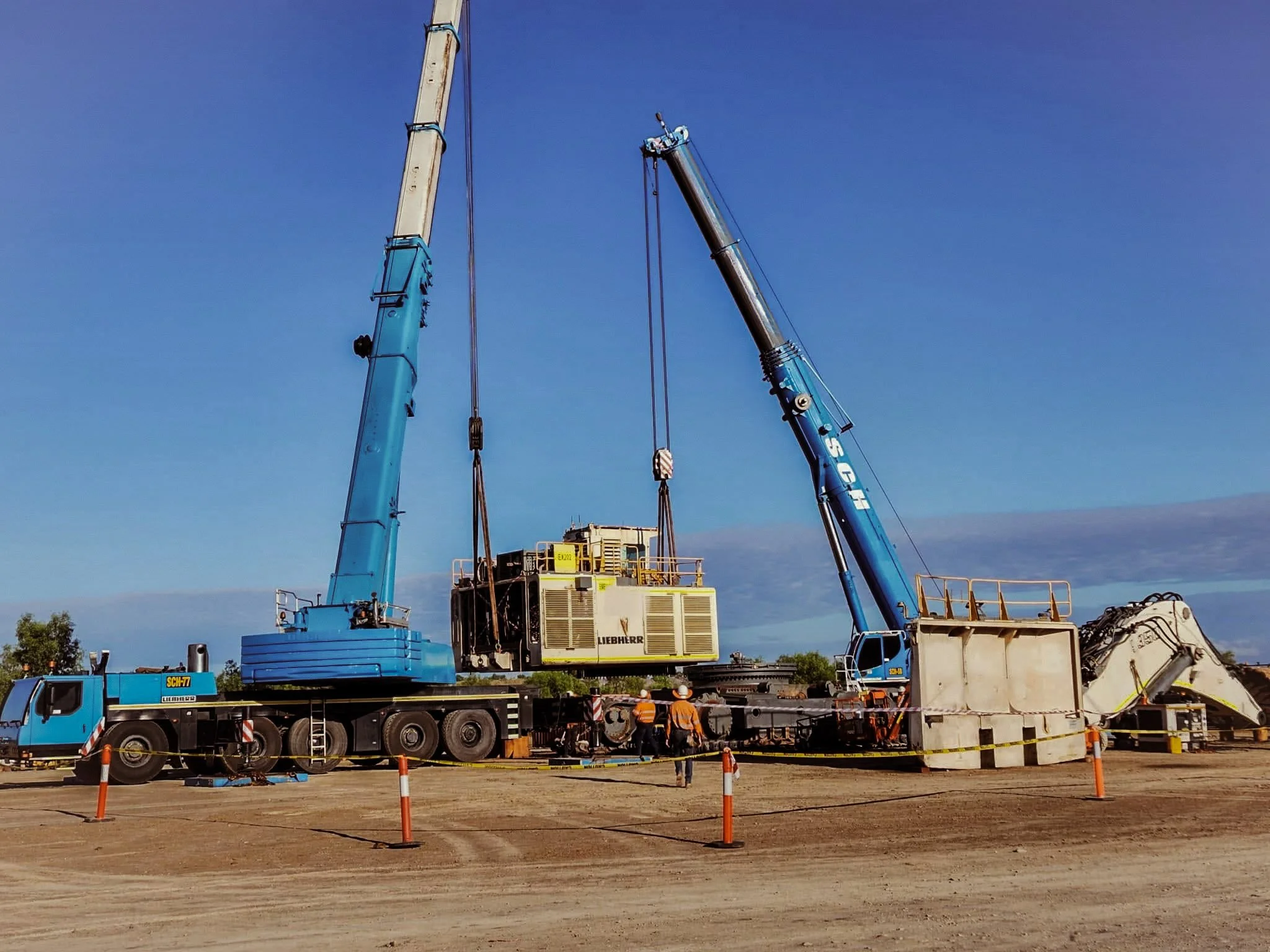 Construction site with multiple cranes and construction workers, with a clear blue sky in the background.
