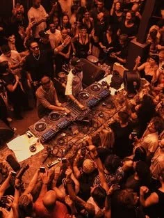 DJ performing at a crowded nightclub with dancing guests surrounding the DJ booth.