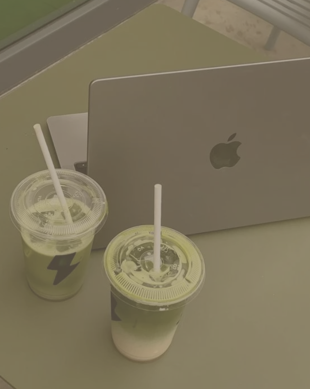 Two green drinks with straws and a laptop on a table.