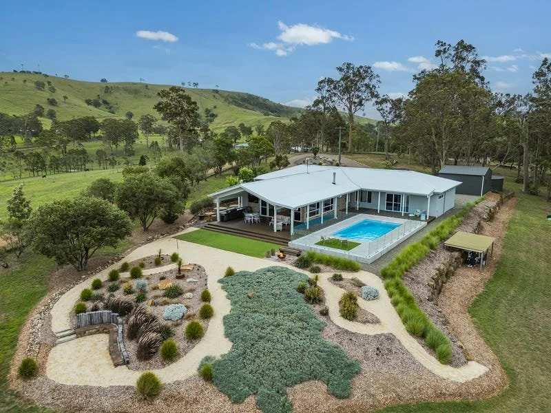 A modern house with a swimming pool surrounded by a landscaped yard and green hills in the background.