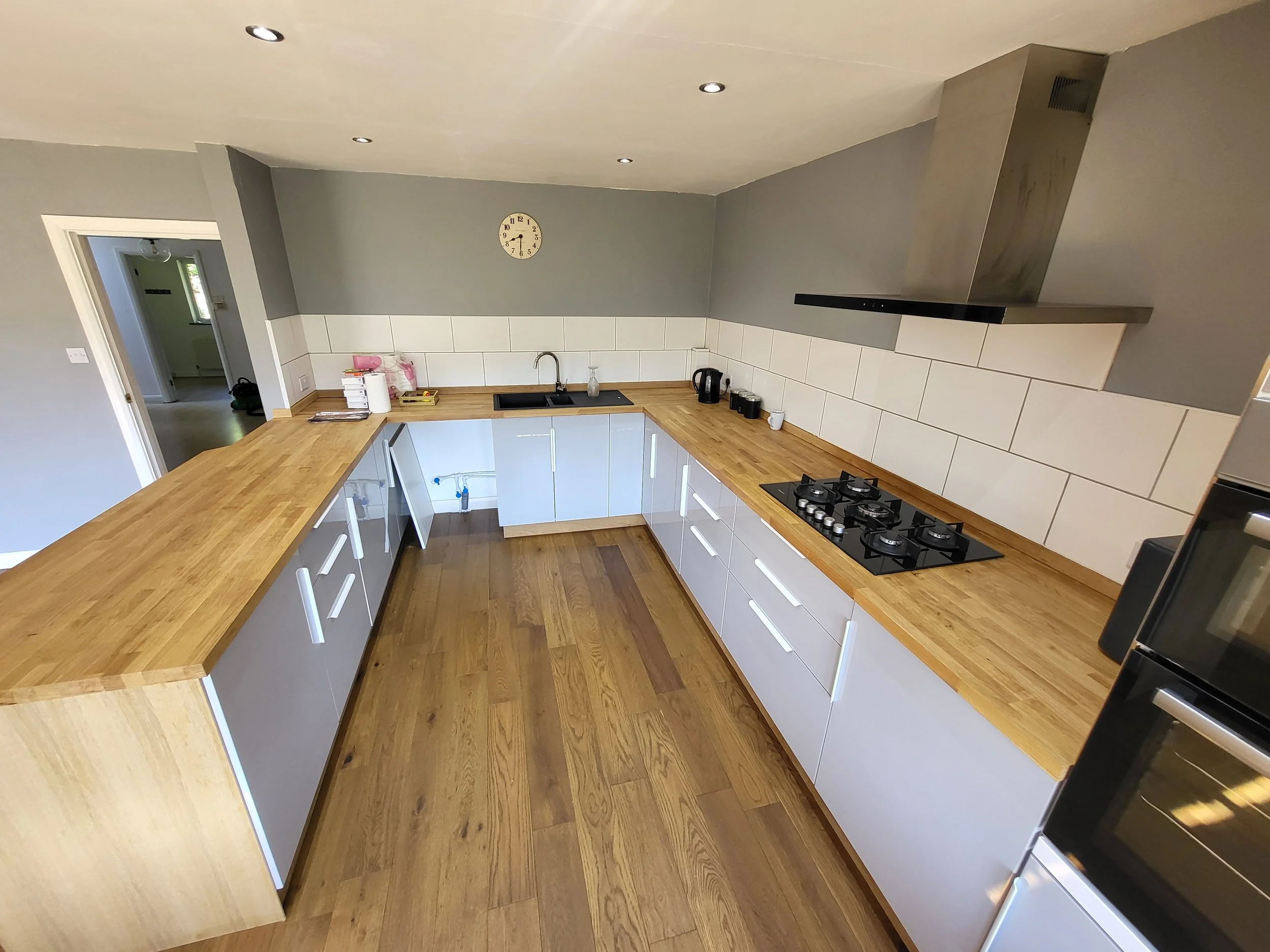 Modern kitchen with wooden countertops, gray cabinets, white tiled backsplash, black stovetop, and stainless steel range hood.