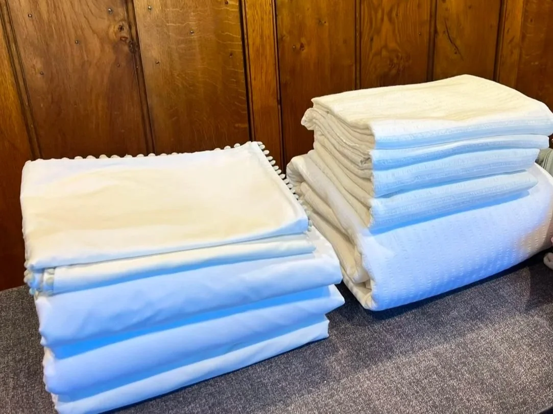 Stacks of folded white mattress pads or bedding on a carpeted floor against a wooden-paneled wall.