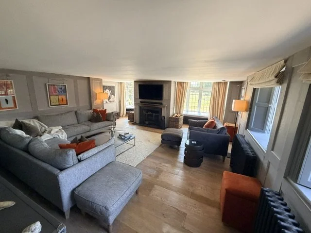 Living room with large sectional sofa, armchair, TV on fireplace, windows with curtains, and various decorative pillows.