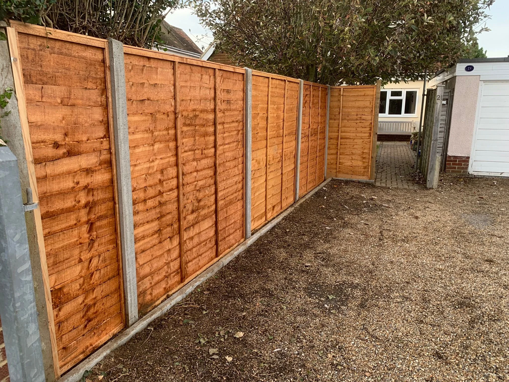 New wooden fence beside a house, with trees in the background and a narrow pathway.