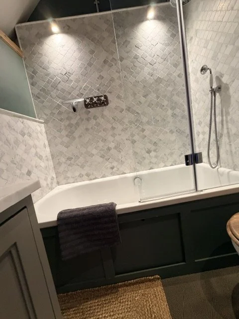 Bathroom with a bathtub, tiled walls, a mounted showerhead, and a towel hanging over the tub's edge.