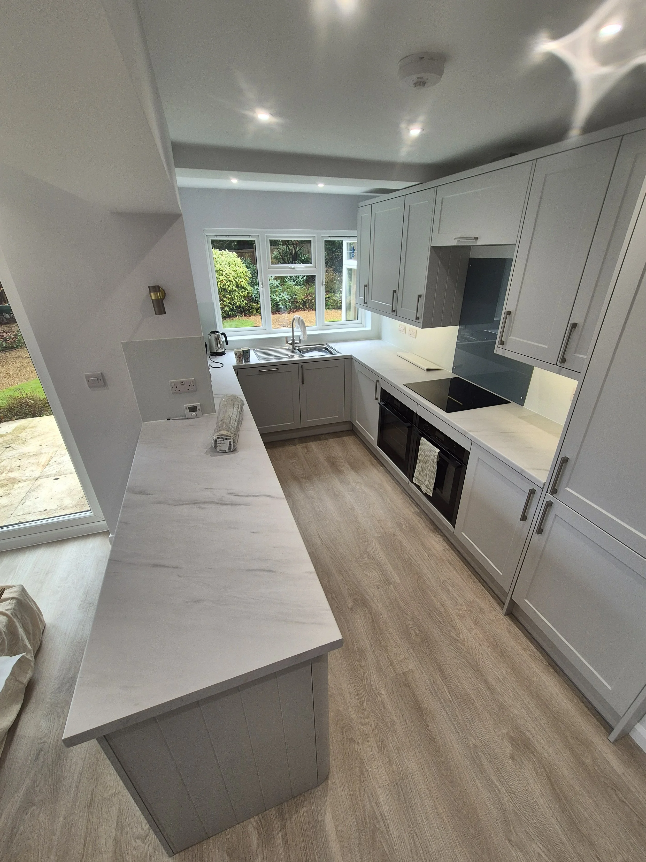 Modern kitchen with white countertops, gray cabinets, a stainless steel sink with a window showing a garden, and an electric stove.