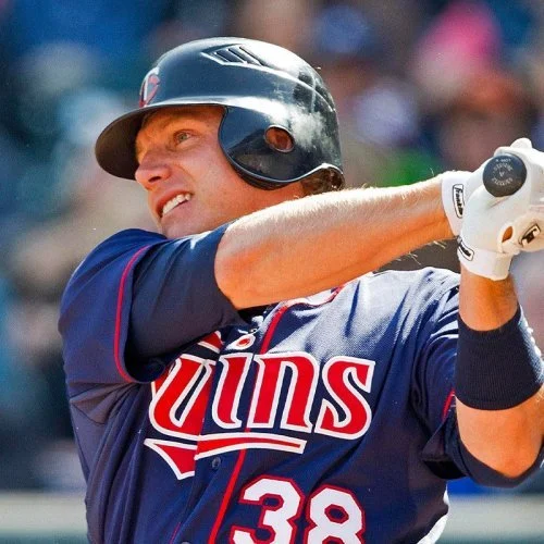 Baseball player in a dark helmet and a navy blue jersey with red and white accents, swinging a bat.