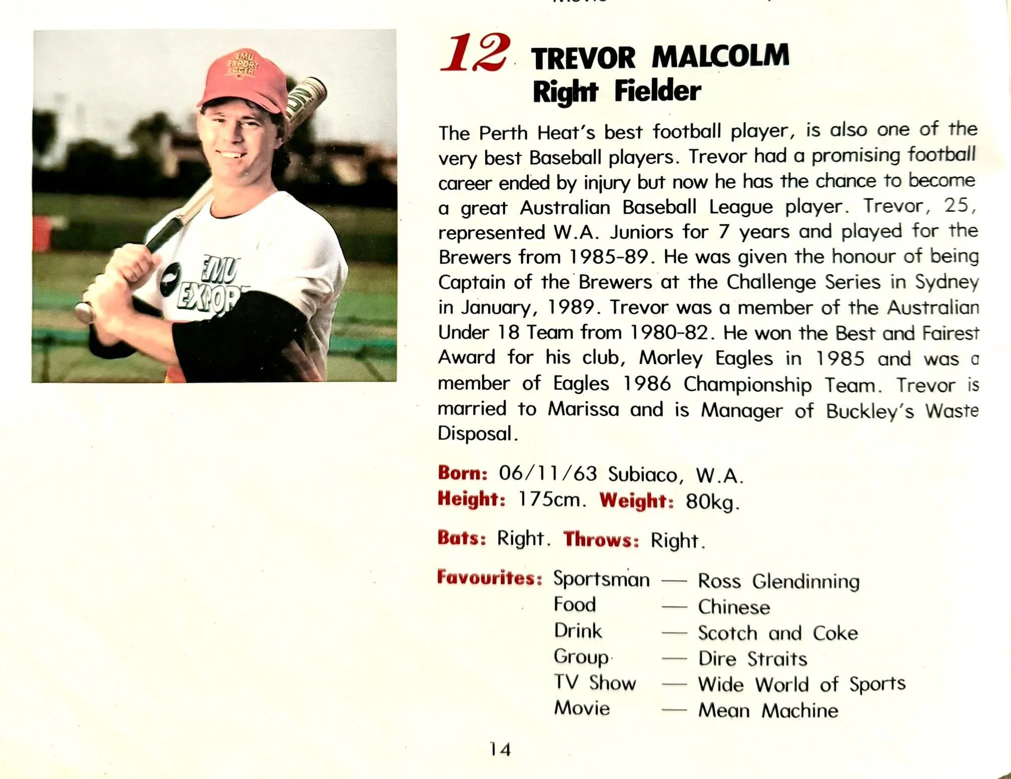 Photograph of a young man wearing a red baseball cap and white shirt, holding a baseball bat, standing on a baseball field with trees in the background.
