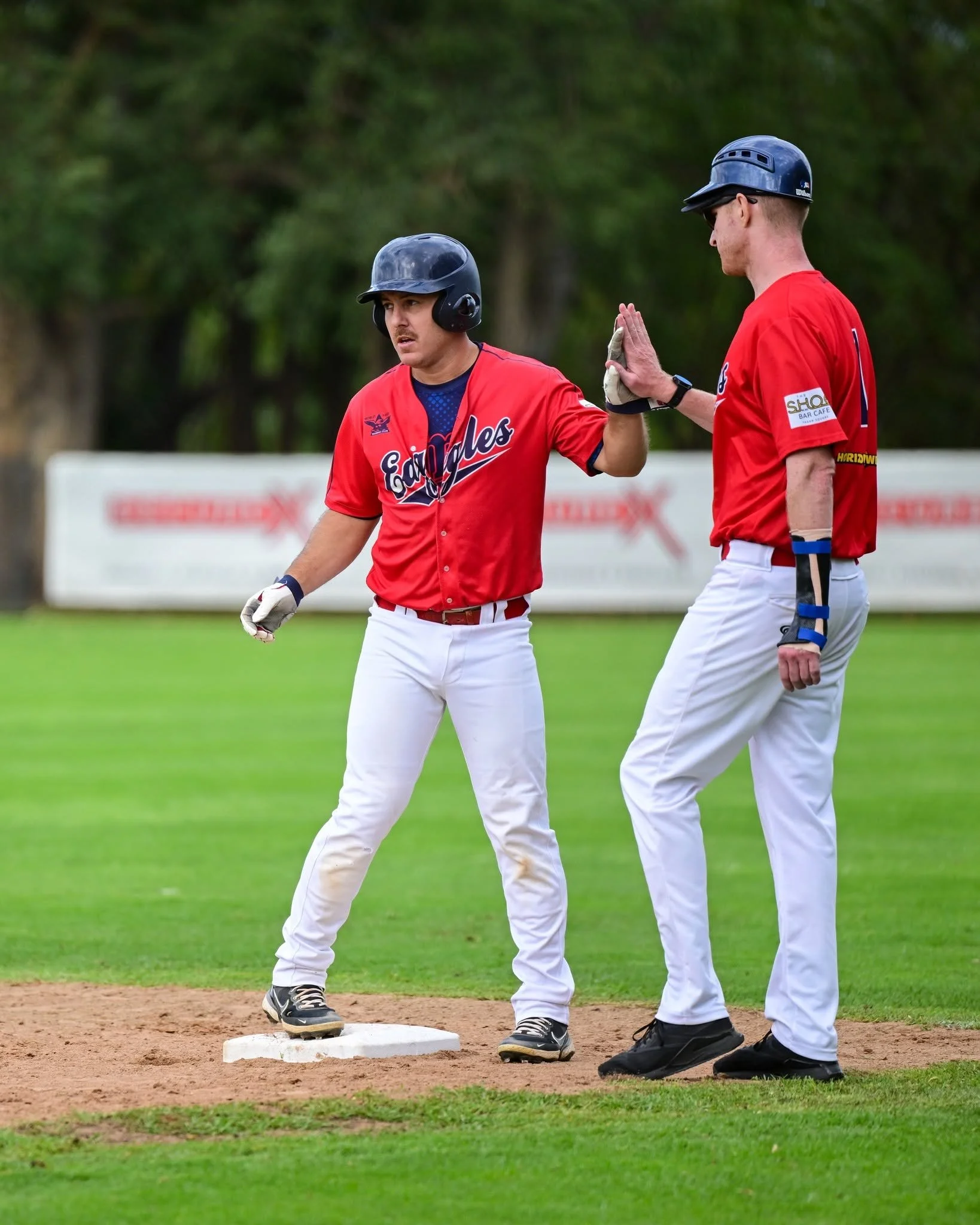 Two baseball players in red uniforms and black helmets giving a high five on a baseball field.