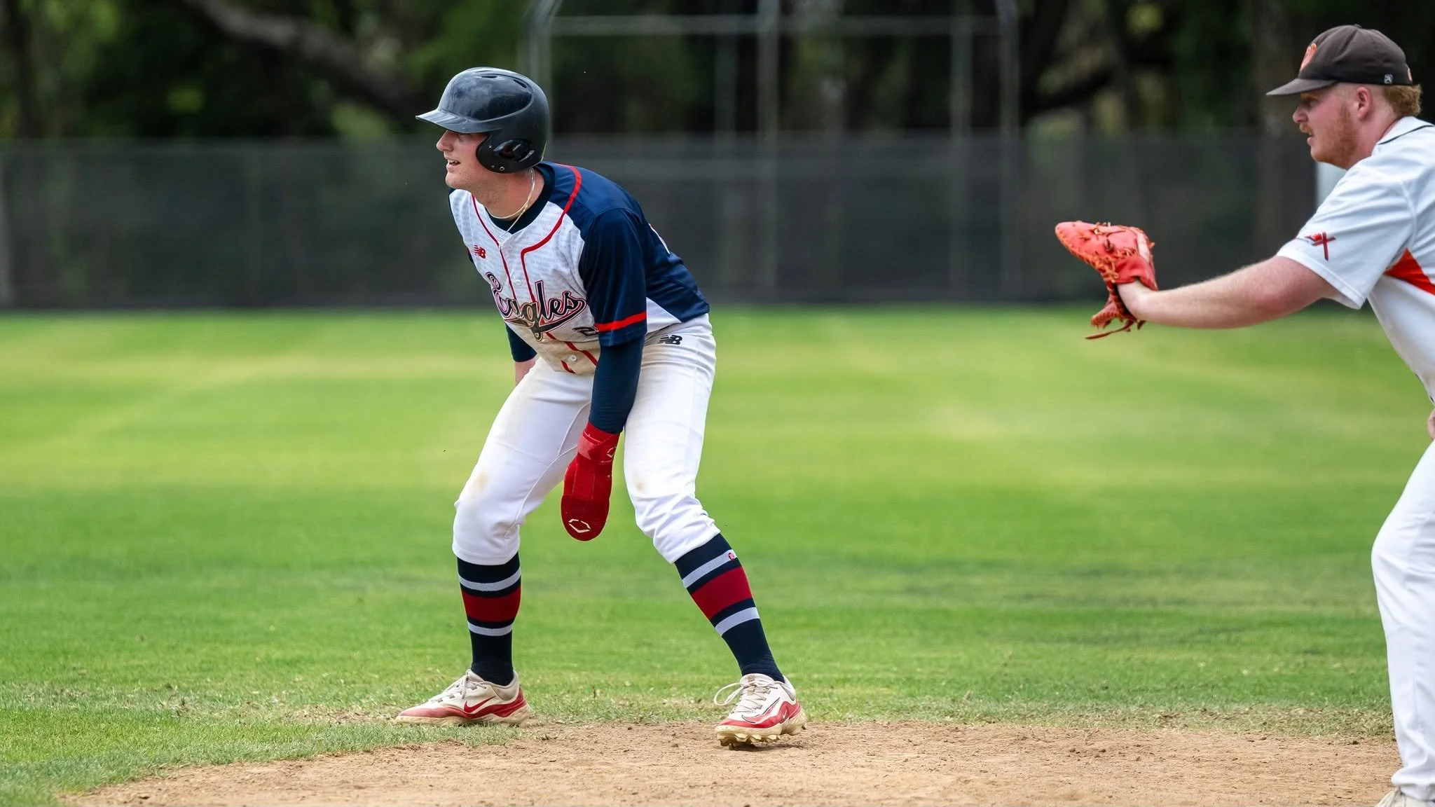 A baseball player in a colorful uniform and helmet stands on the base path, ready for the next move, with another player in a white uniform and cap accurately catching a ball.