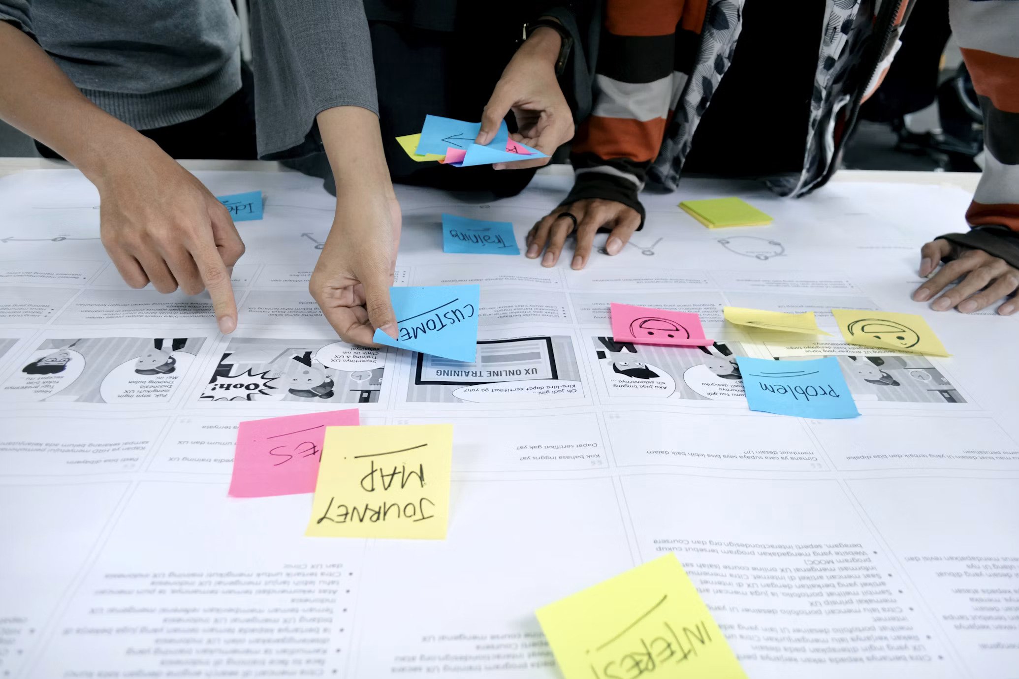Close-up of multiple hands pointing to documents on a table with colorful sticky notes containing handwritten words.