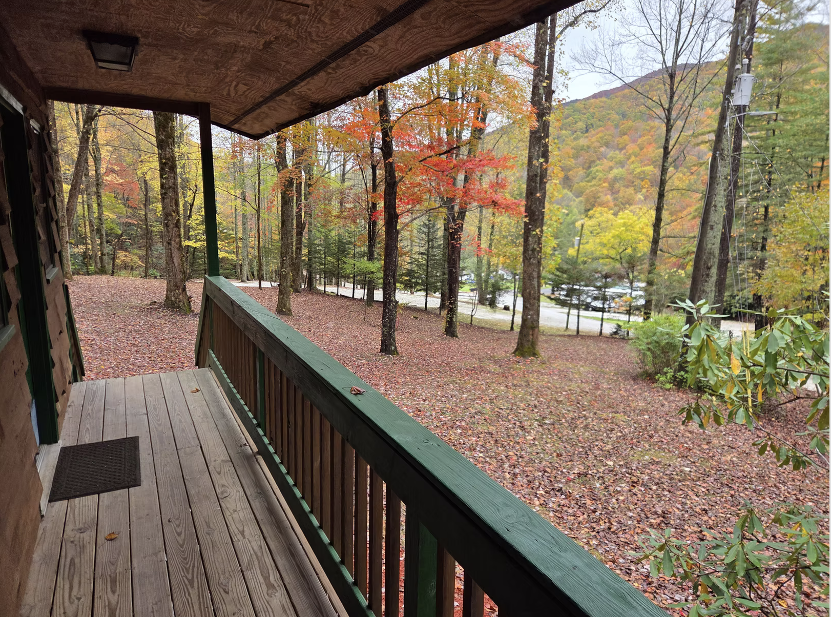 Covered cabin porch with a wooden railing overlooking fall trees