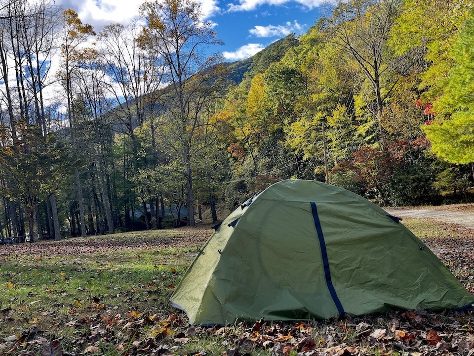Green dome tent at a wooded mountain campsite surrounded by autumn foliage