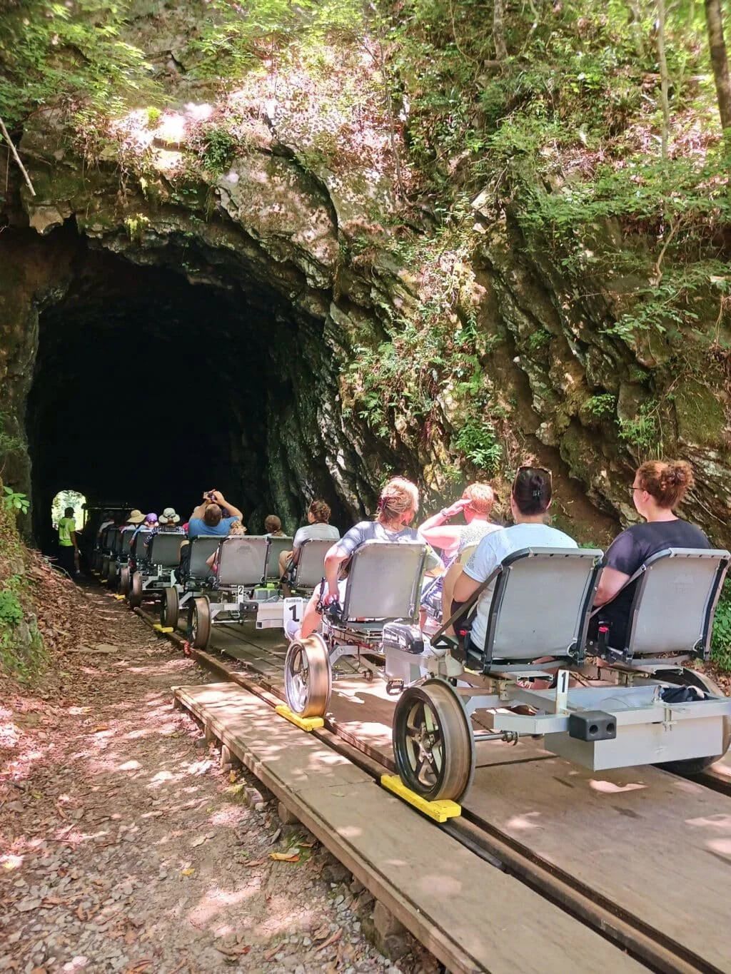 Riders on open-air rail bikes heading into a mountain tunnel