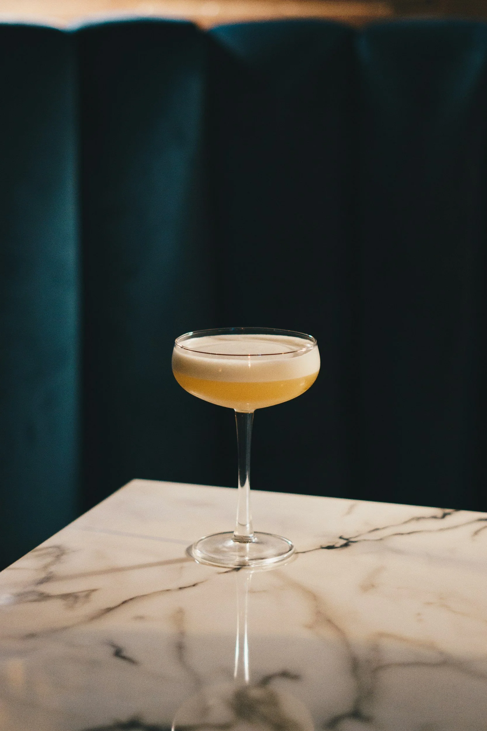 Cocktail in een coupe glas op een witte marmeren tafel.