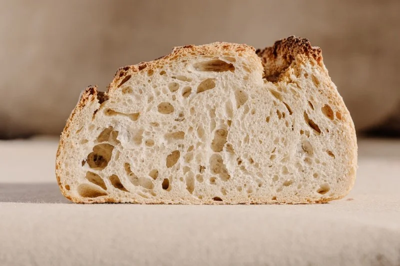 Een stuk brood met een krokante korst en een open, luchtige binnenkant, op een neutrale achtergrond.