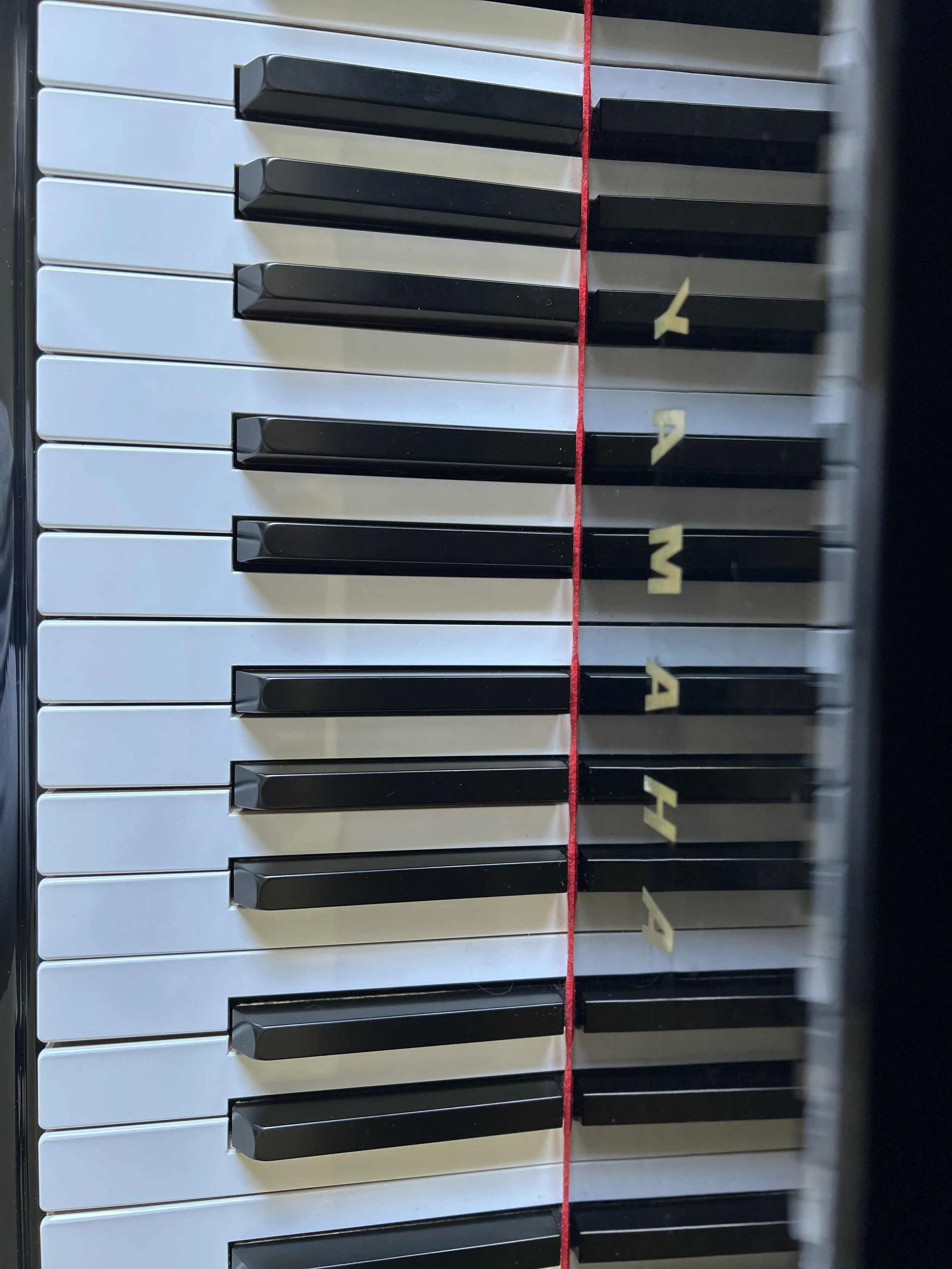 Close-up of a piano keyboard with black and white keys, with a red string and yellow sticky notes numbered 1, 2, and 3 along the right side of the keyboard.