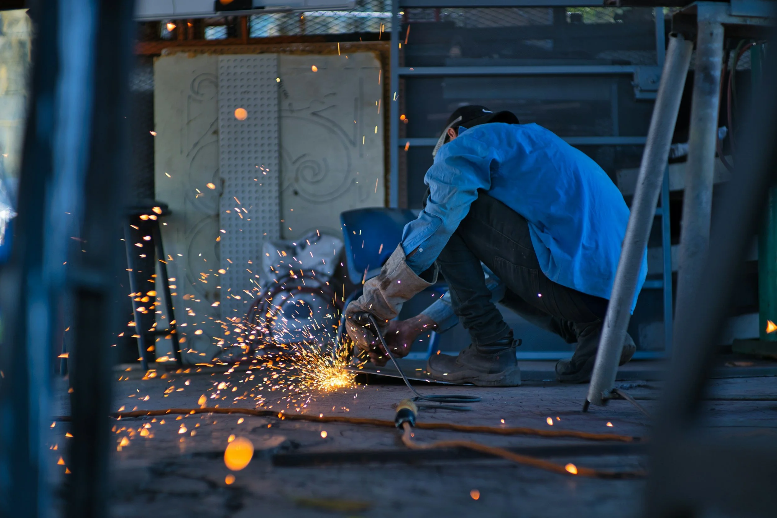 A worker welding metal on a construction site, sparks flying as he crouches down.