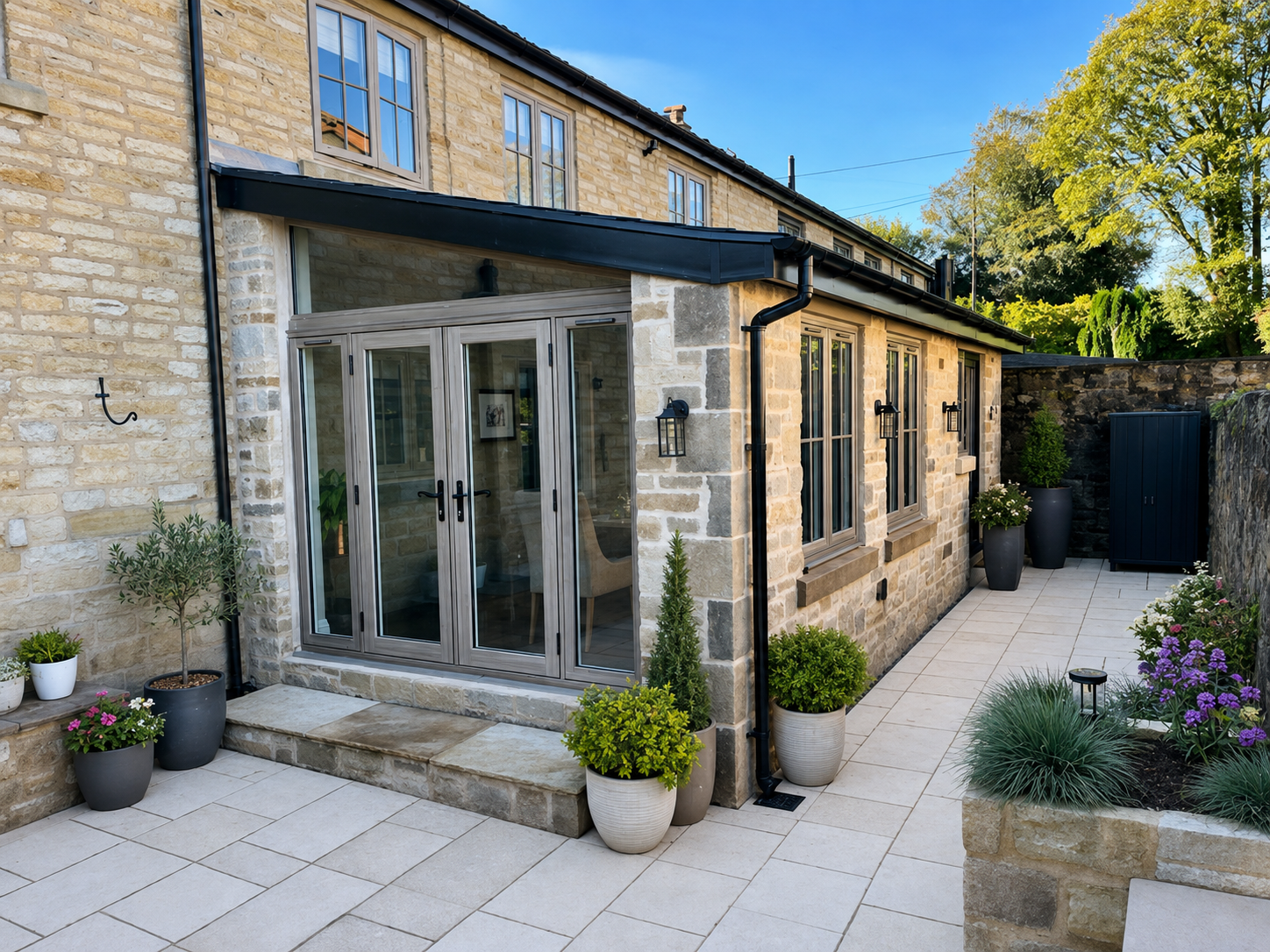 A modern outdoor patio area with potted plants, a stone pathway, and a brick house with large windows and a glass door.