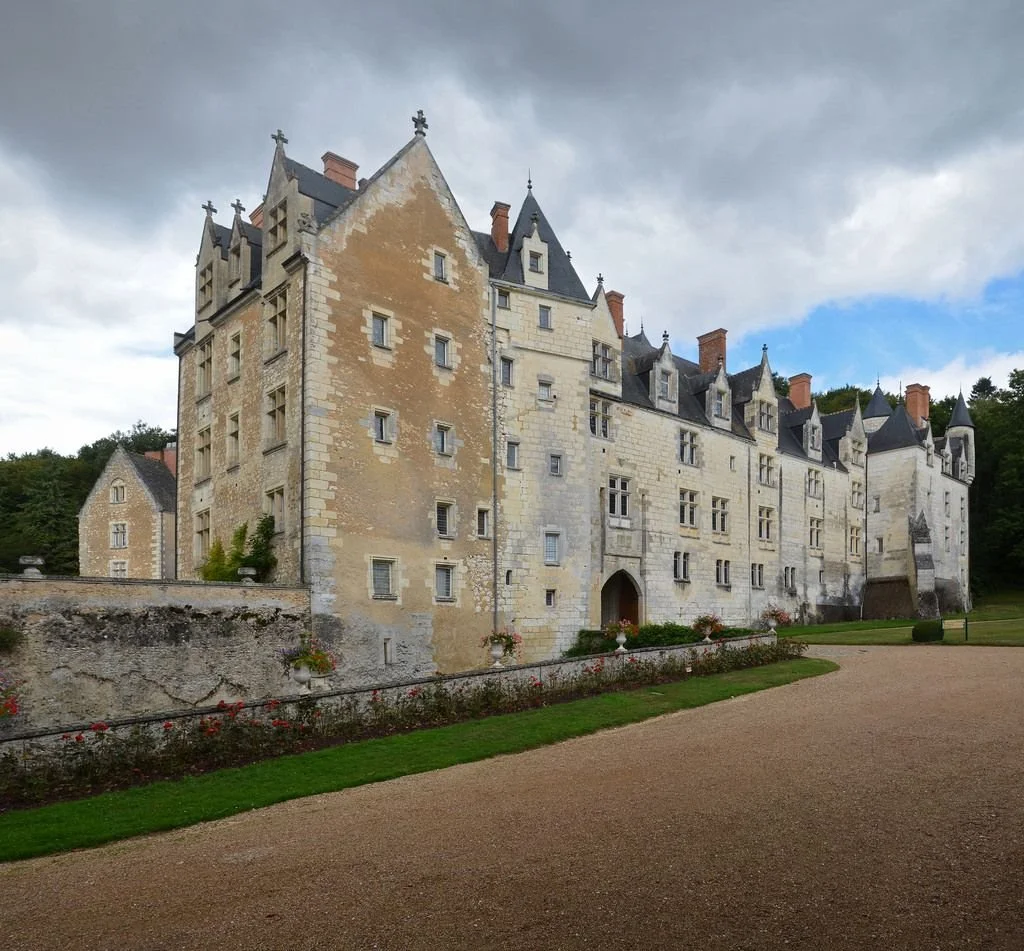 un château médiéval en pierre avec plusieurs tours pointues et fenêtres, entouré d'un jardin bien entretenu avec un chemin en gravier
