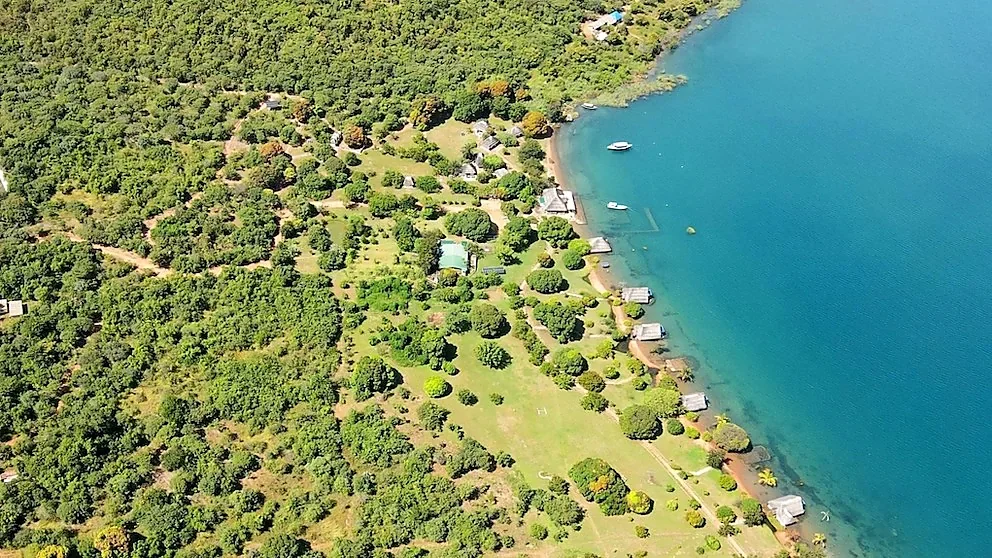 Aerial view of Lake Shore Lodge in Kipili, Tanzania, showing lakeside bandas, landscaped gardens and natural woodland beside the turquoise waters of Lake Tanganyika.
