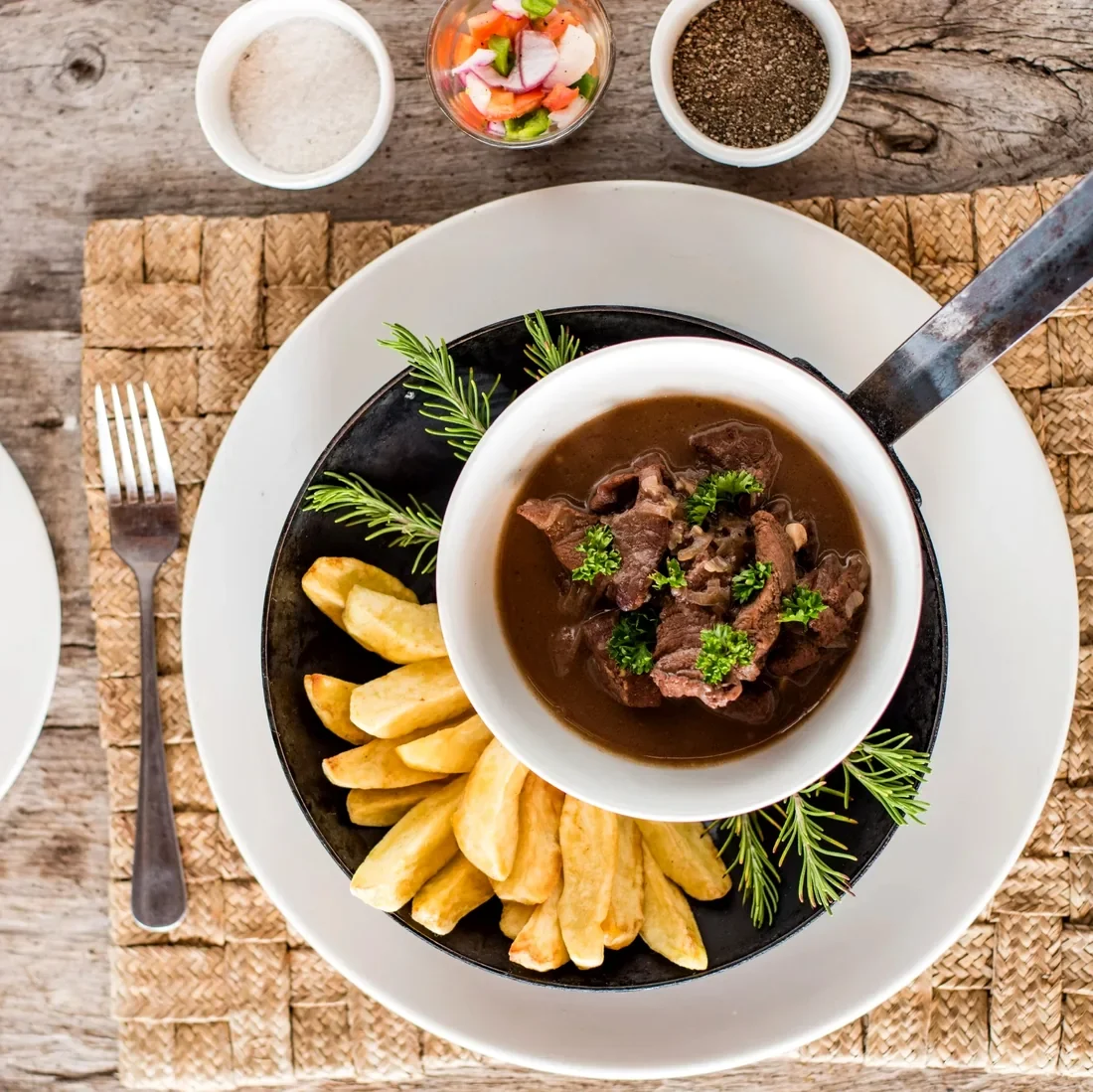 Steak trinchado served in a rich sauce with golden chips and fresh herb garnish at Lake Shore Lodge restaurant, Lake Tanganyika, Tanzania.