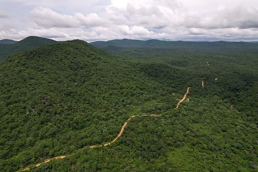 Aerial view of a winding red-earth road through the forested hills of Luafi Game Reserve on the scenic drive from Sumbawanga to Lake Shore Lodge, Lake Tanganyika, Tanzania.