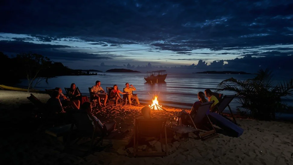 Guests relaxing around a beach fire at Lake Shore Lodge on Lake Tanganyika at dusk