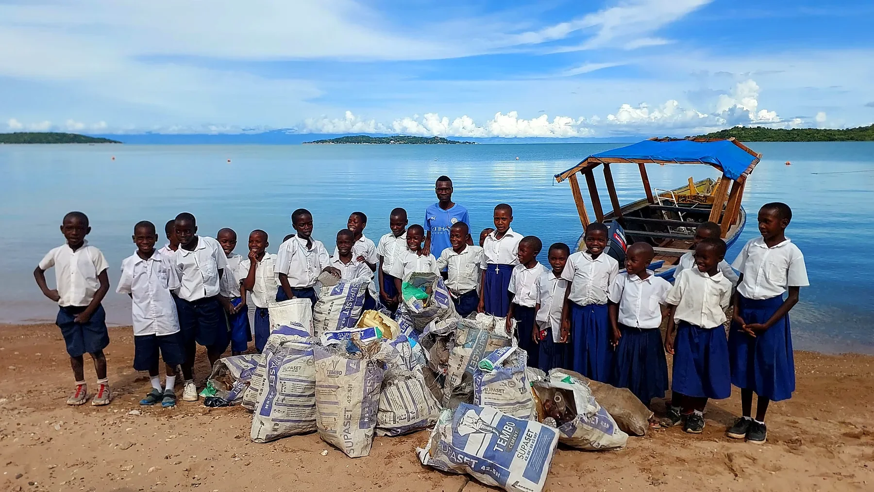 Schoolchildren in Kipili, Tanzania, standing beside bags of collected rubbish following a community cleanup on the shores of Lake Tanganyika.