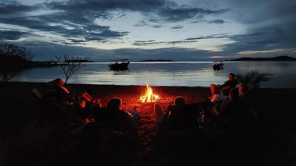 Guests relaxing around a beach fire at Lake Shore Lodge overlooking Lake Tanganyika at dusk.