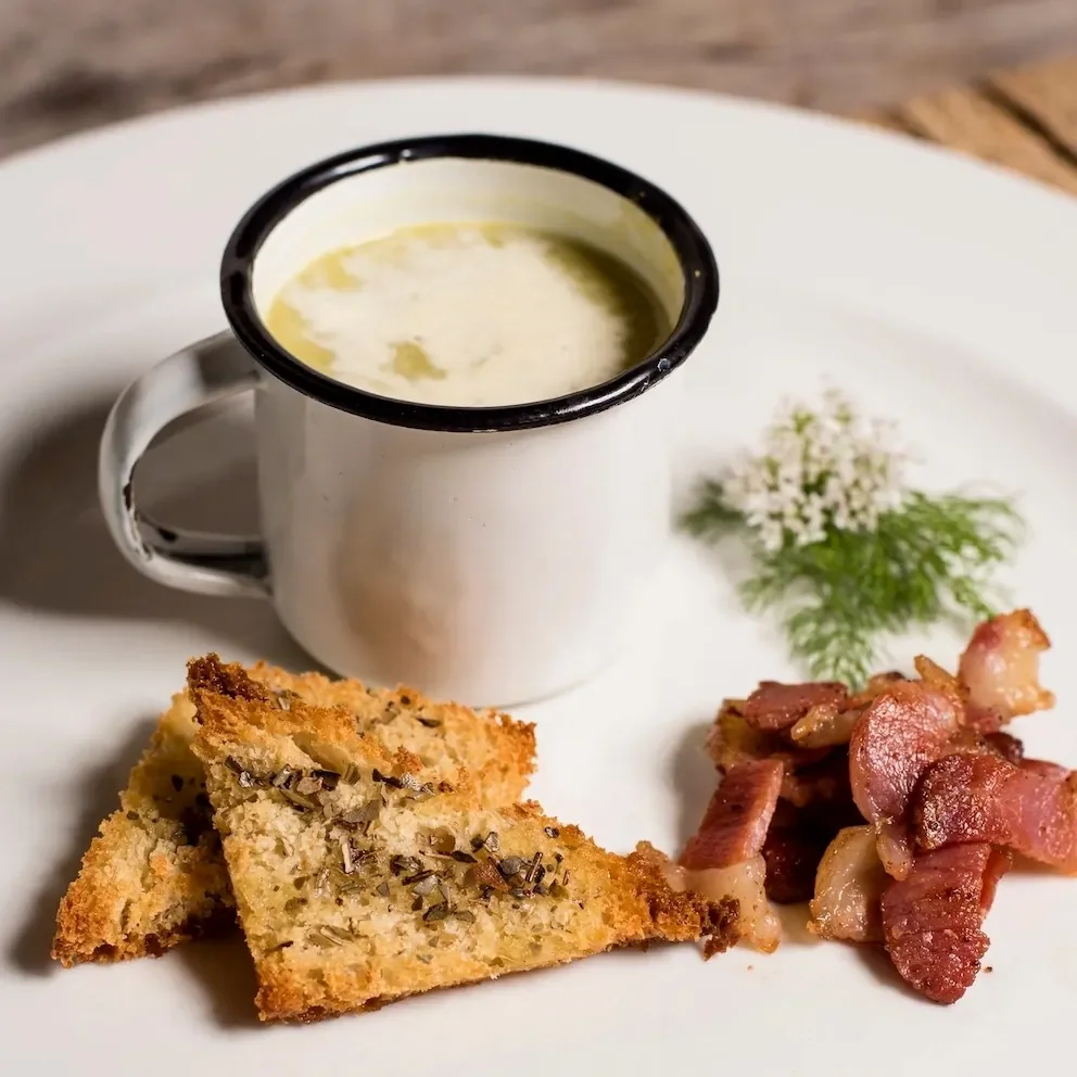 Creamy soup served in a rustic enamel mug with herb croutons and crispy bacon at Lake Shore Lodge restaurant, Lake Tanganyika, Tanzania.