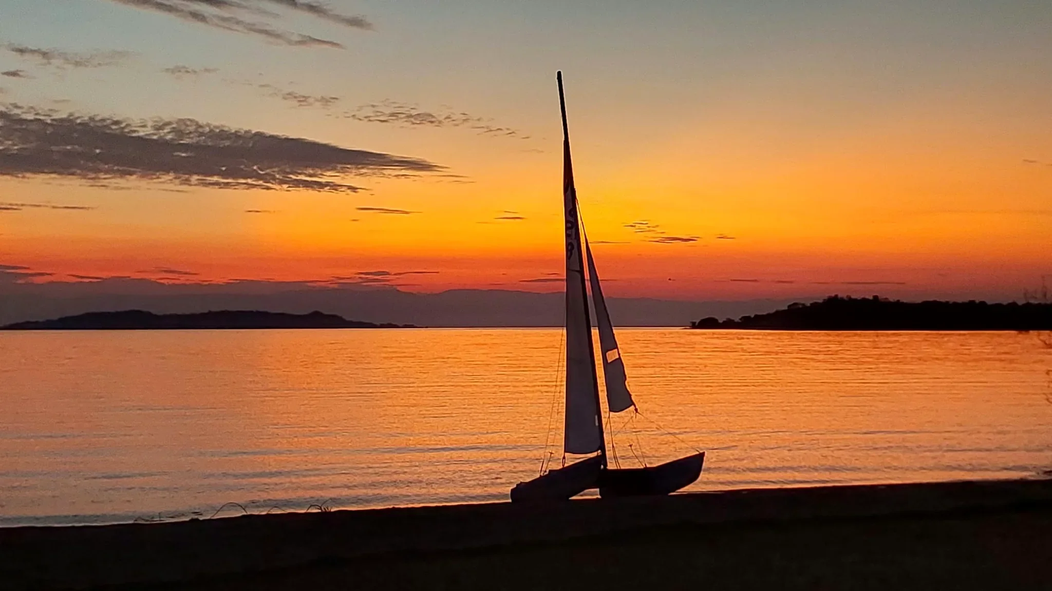Sailing catamaran silhouetted against a spectacular orange sunset over Lake Tanganyika at Lake Shore Lodge, Tanzania.