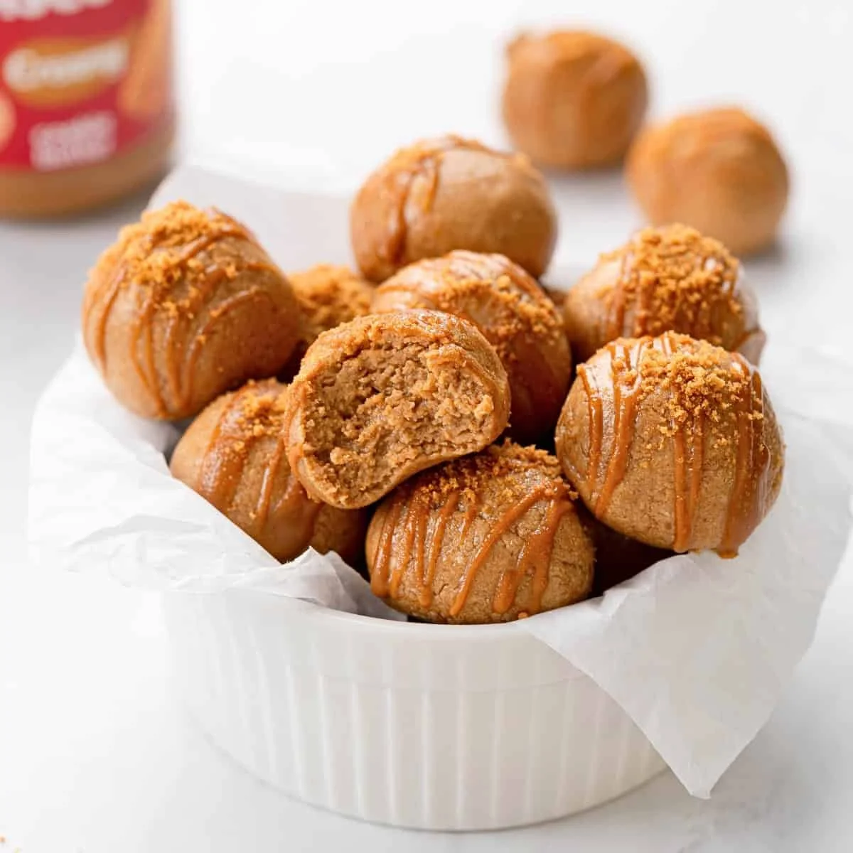 A white bowl filled with caramel-flavored cookie dough bites topped with caramel drizzle and crushed cookie crumbs.