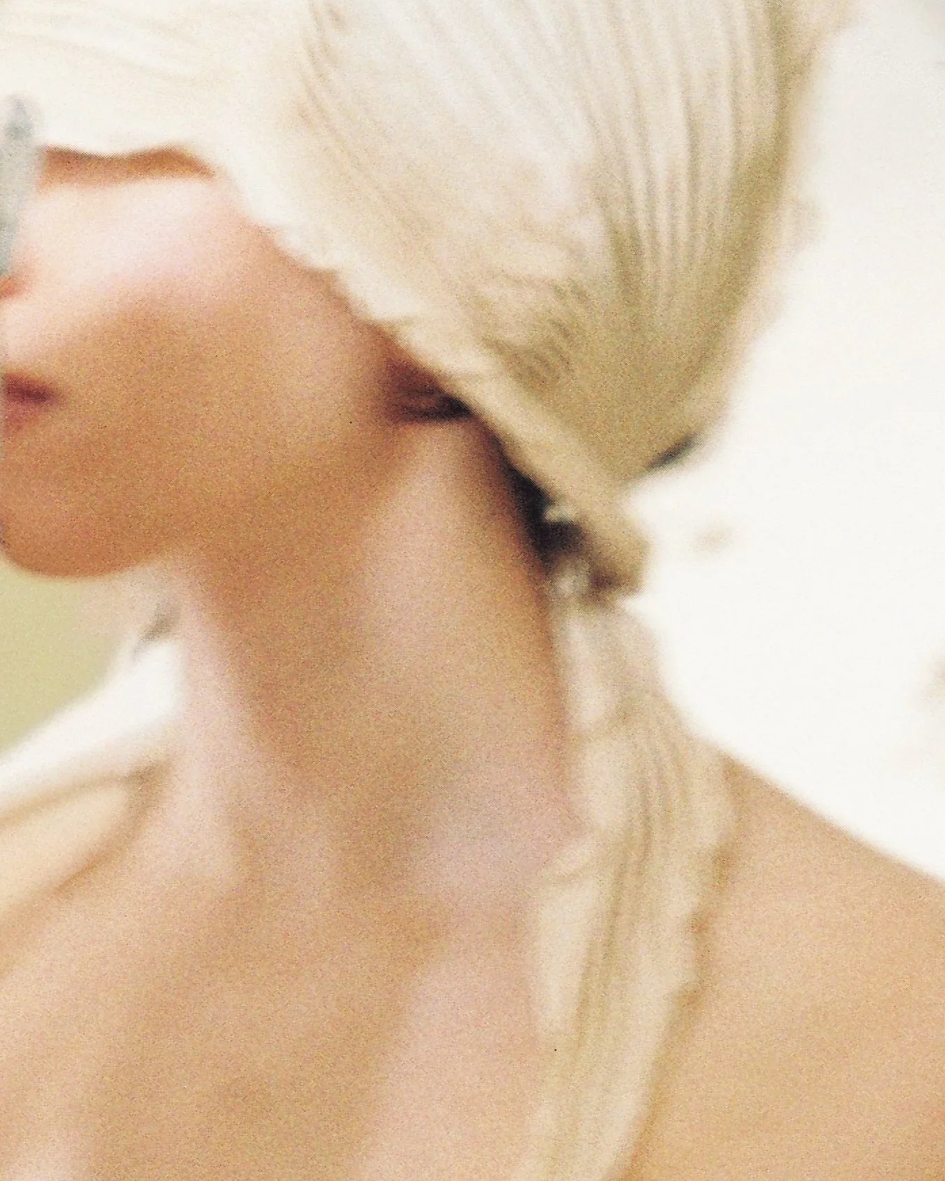 Close-up of a person with blonde hair, their face partially visible, and hand touching their neck or collarbone.
