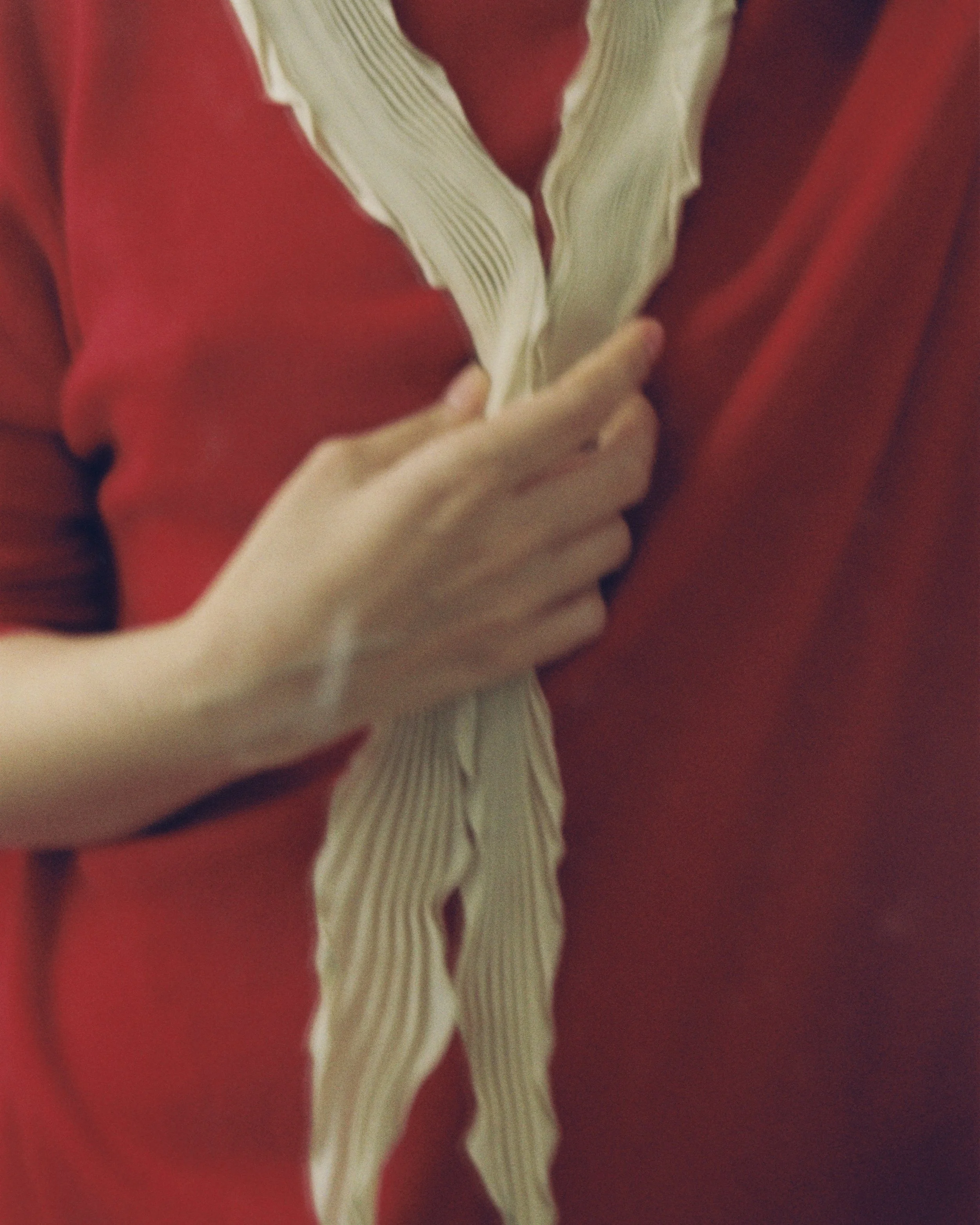 Close-up of a person's hand holding Soeur pleated scarf wearing a red sweater.