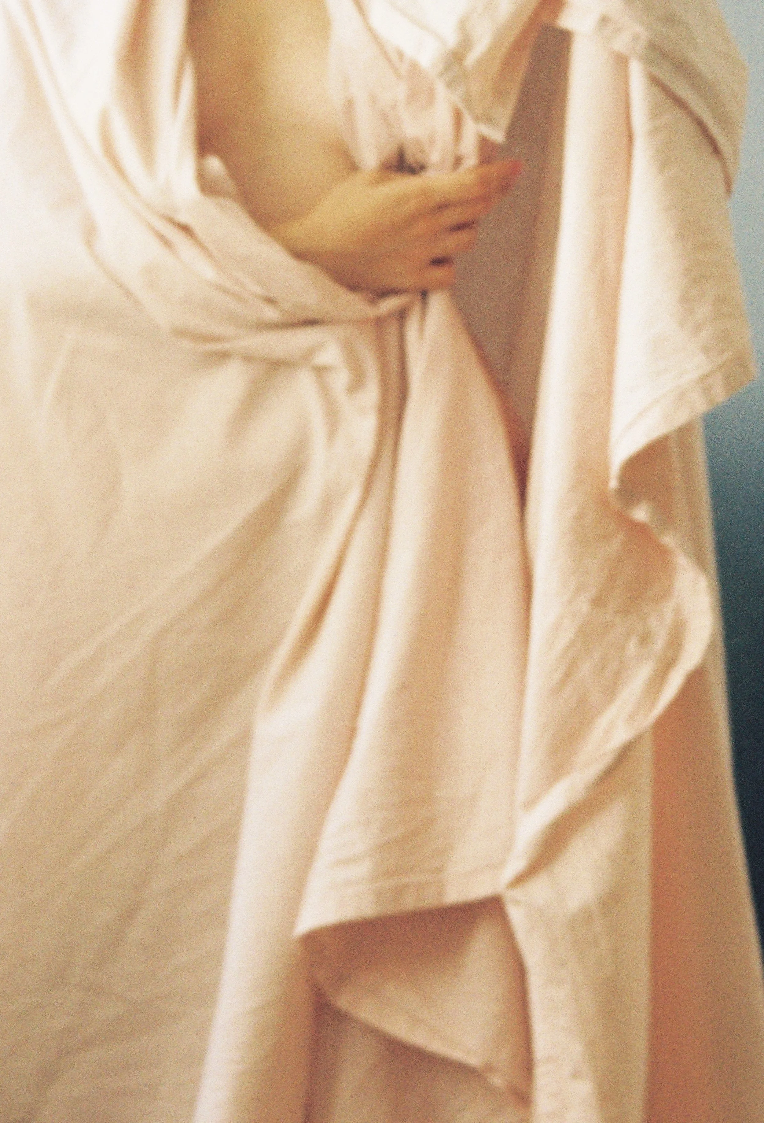 Close-up of a person wearing a light beige or cream-colored shirt, with buttons, slightly unbuttoned at the top. The person's hand is partially visible, resting on their chest.