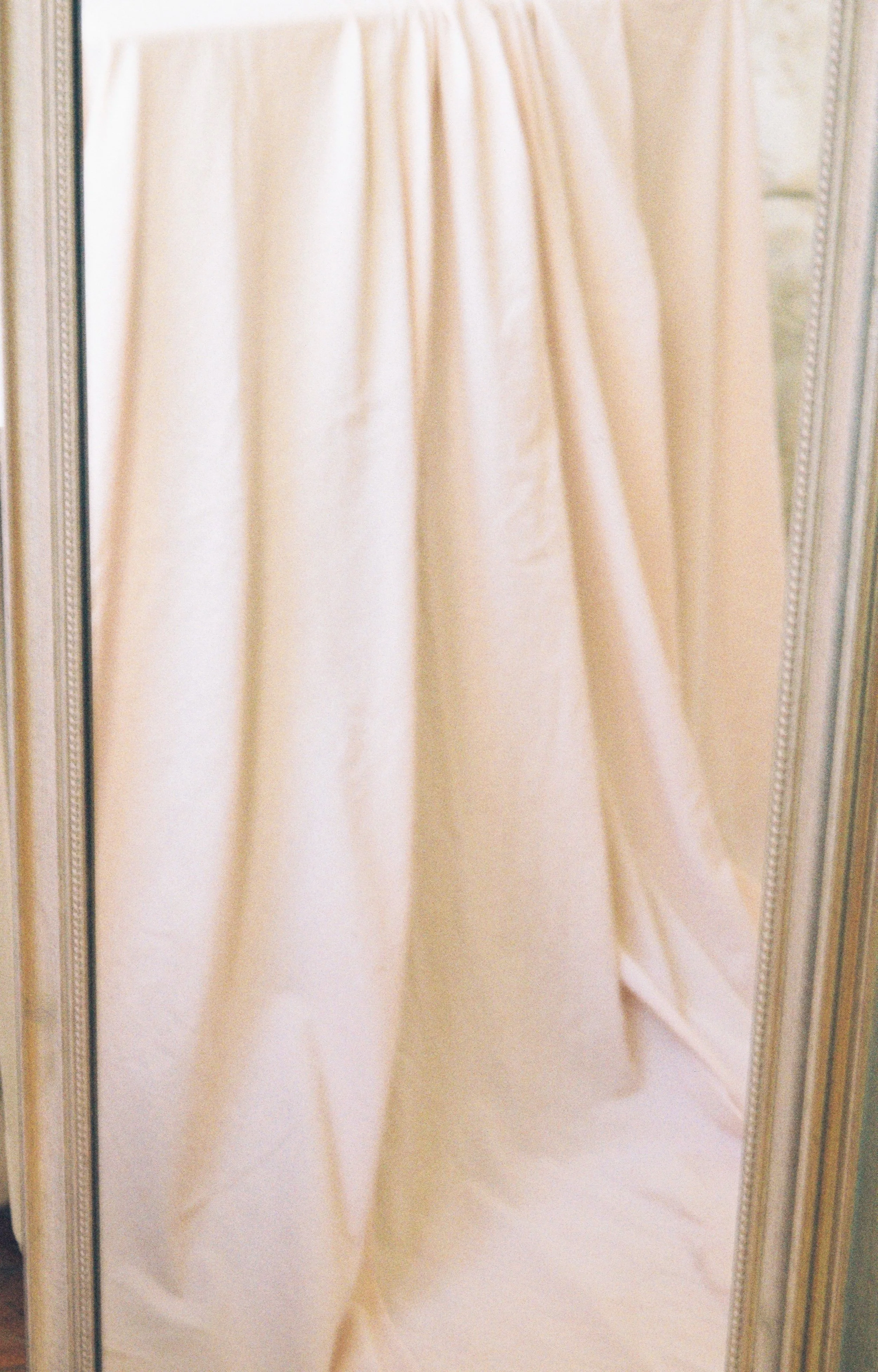 Pink curtains hanging in front of a mirror with decorative border.