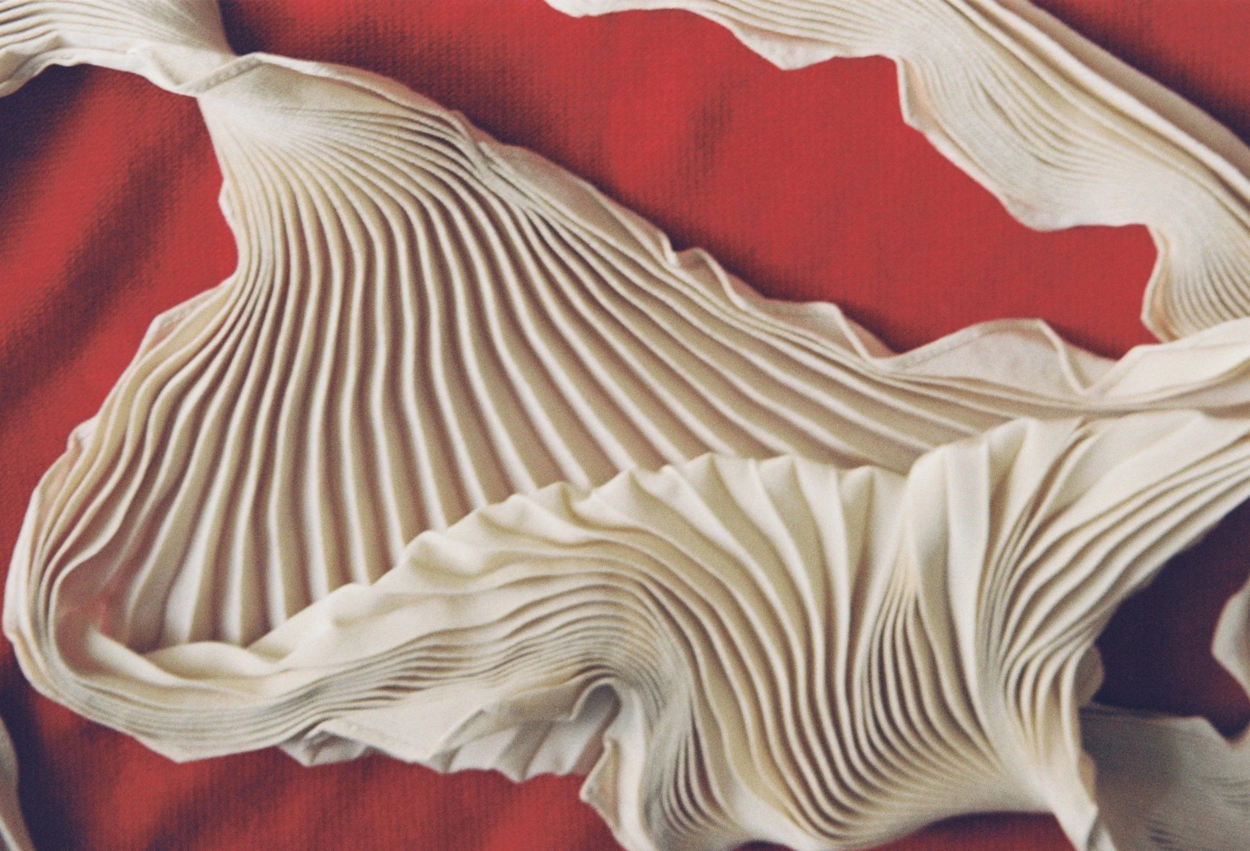 Pleated cream Soeur scarf arranged on a red fabric background.